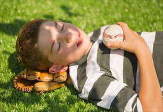 Boy (10-11) holding baseball and baseball glove lying on grass. Photo : Daniel Grill