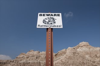 USA, South Dakota, Badlands National Park, Rattlesnake warning sign against sky, mountain in background.