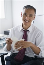 Portrait of smiling businessman holding Chinese take away. Photo : Jamie Grill