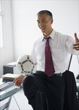 Smiling businessman kicking ball in office. Photo : Jamie Grill