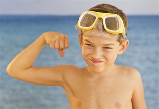 Boy (10-11) wearing swimming goggles flexing muscles. Photo : Daniel Grill