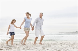 Parents with daughter (10-11) walking on beach. Photo : Momentimages