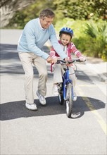 Grandfather helping granddaughter (10-11) riding bike. Photo : Momentimages