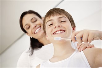 Mother embracing son (12-13) while he is brushing teeth. Photo : Momentimages