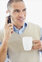 Office worker holding mobile phone in one hand and cup in another. Photo : Momentimages