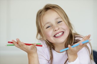 Girl (10-11) gesturing with red and blue pencils. Photo : Momentimages