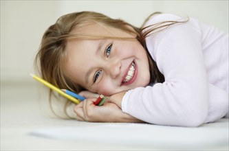 Girl (10-11) laying on side with yellowblue and red pencils. Photo : Momentimages