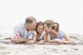 Two parents lying on beach with daughter (10-11). Photo : Momentimages
