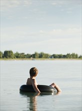 Boy (12-13) floating on rubber ring on lake.