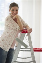 Young woman with paint roller on ladder .
