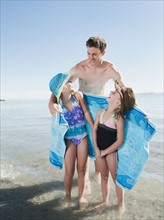 Portrait of girls (6-7,8-9) wrapped in towel on beach with their father.