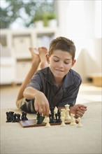 Boy (10-11) lying on floor and playing chess. Photo : Daniel Grill