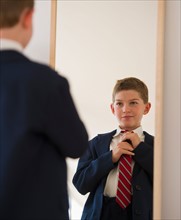 Boy (10-11) adjusting tie in front of mirror. Photo : Daniel Grill