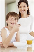 Mother embracing son (12-13) while he is eating breakfast. Photo : Momentimages