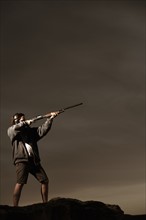 Man aiming rifle on rocks. Photo : Shawn O'Connor