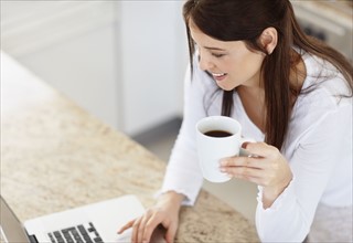 Mid adult woman using laptop in kitchen. Photo : Momentimages