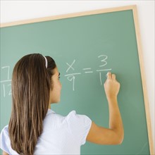 Girl (12-13) writing on chalk board in class.