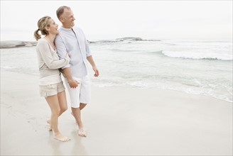 Couple holding hands and walking on empty beach. Photo : Momentimages