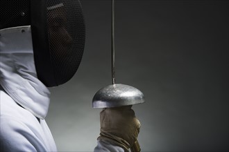 Studio portrait of fencer holding fencing foil.