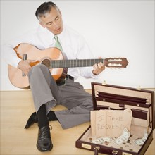 Businessman playing guitar in office. Photo : Jamie Grill