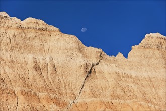 USA, South Dakota, Mountain against blue sky with moon in Badlands National Park.