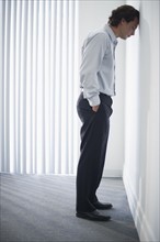 Man in office leaning head against wall.