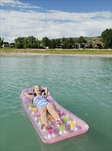 Girl (8-9) floating on inflatable bed.