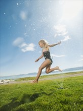 Girl (8-9) jumping over watering system.