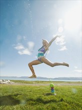 Girl (8-9) jumping over watering system.