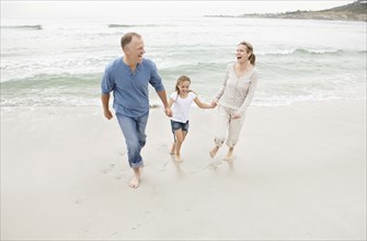 Smiling family holding hands and walking on beach. Photo : Momentimages