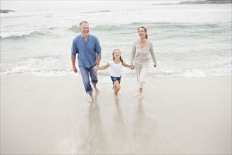 Smiling family holding hands and walking on beach. Photo : Momentimages