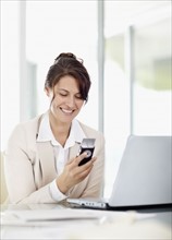 Businesswoman using phone in office. Photo : Momentimages