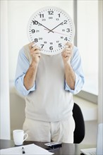 Office worker holding clock in front of face. Photo : Momentimages