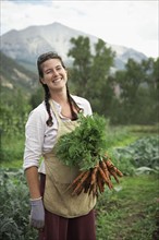 Portrait of woman holding carrots in field. Photo : Shawn O'Connor
