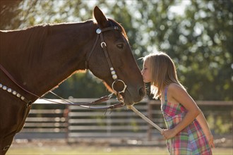Cowgirl (8-9) kissing horse in ranch. Photo : Mike Kemp