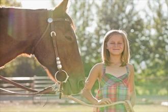 Portrait of smiling cowgirl (8-9) with horse in ranch. Photo : Mike Kemp