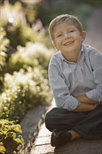 Portrait of boy (6-7) sitting on garden path. Photo : FBP