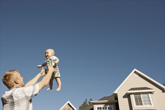 Father lifting baby boy (6-11 months) outside home. Photo : FBP