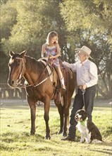 Senior man with dog assisting granddaughter (8-9) horseback riding in ranch. Photo : Mike Kemp