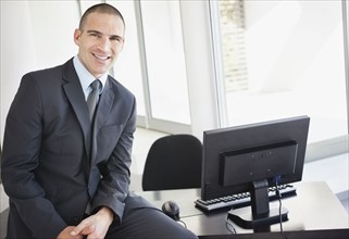 Businessman sitting on office desk. Photo : Momentimages