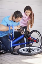 Father with daughter (10-11) fixing bike. Photo : Momentimages