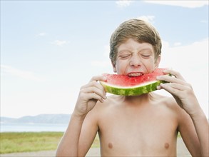 Boy (12-13) eating watermelon.