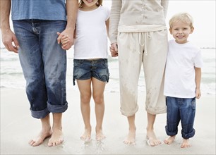 Family holding hands and posing at beach, midsection. Photo : Momentimages