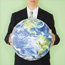 Businessman holding globe, studio shot. Photo : Jamie Grill