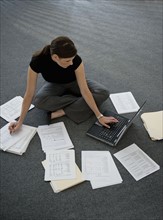 Woman sitting on floor with laptop with documents around.