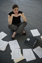 Woman sitting on floor with laptop with documents around.