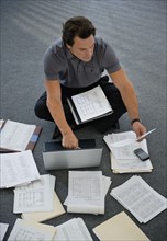 Man sitting on floor with laptop with documents around.