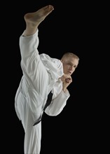 Young man performing karate kick on black background.
