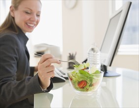 USA, New Jersey, Jersey City, young businesswoman eating salad in office. Photo : Jamie Grill