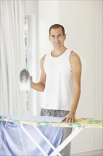 South Africa, Portrait of young man ironing shirt. Photo : momentimages